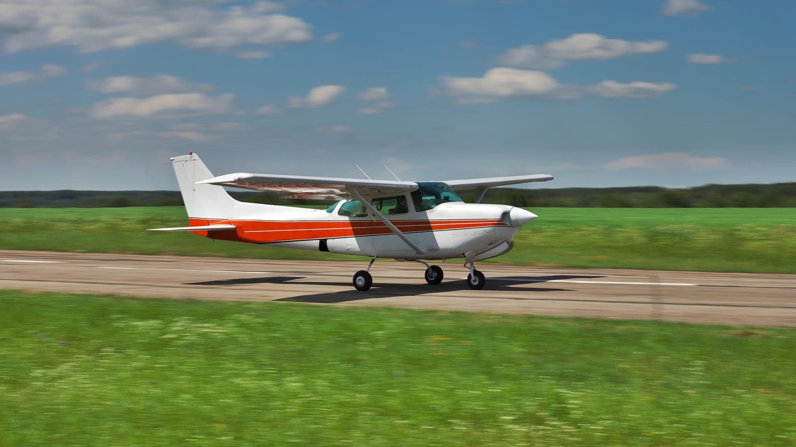A single red and white Cessna on an empty runway beside open grass
