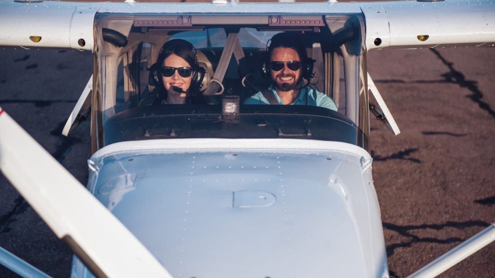 Two club members in sunglasses sitting side by side in the open cockpit of a low-wing aircraft on the ramp