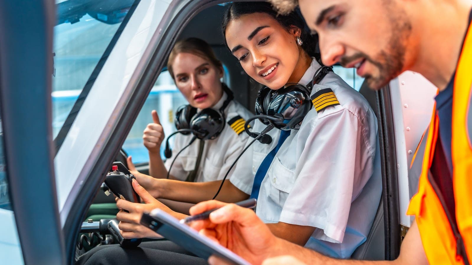 Three people around the open door of a light aircraft, one holding a tablet while another gives a thumbs up from the pilot seat