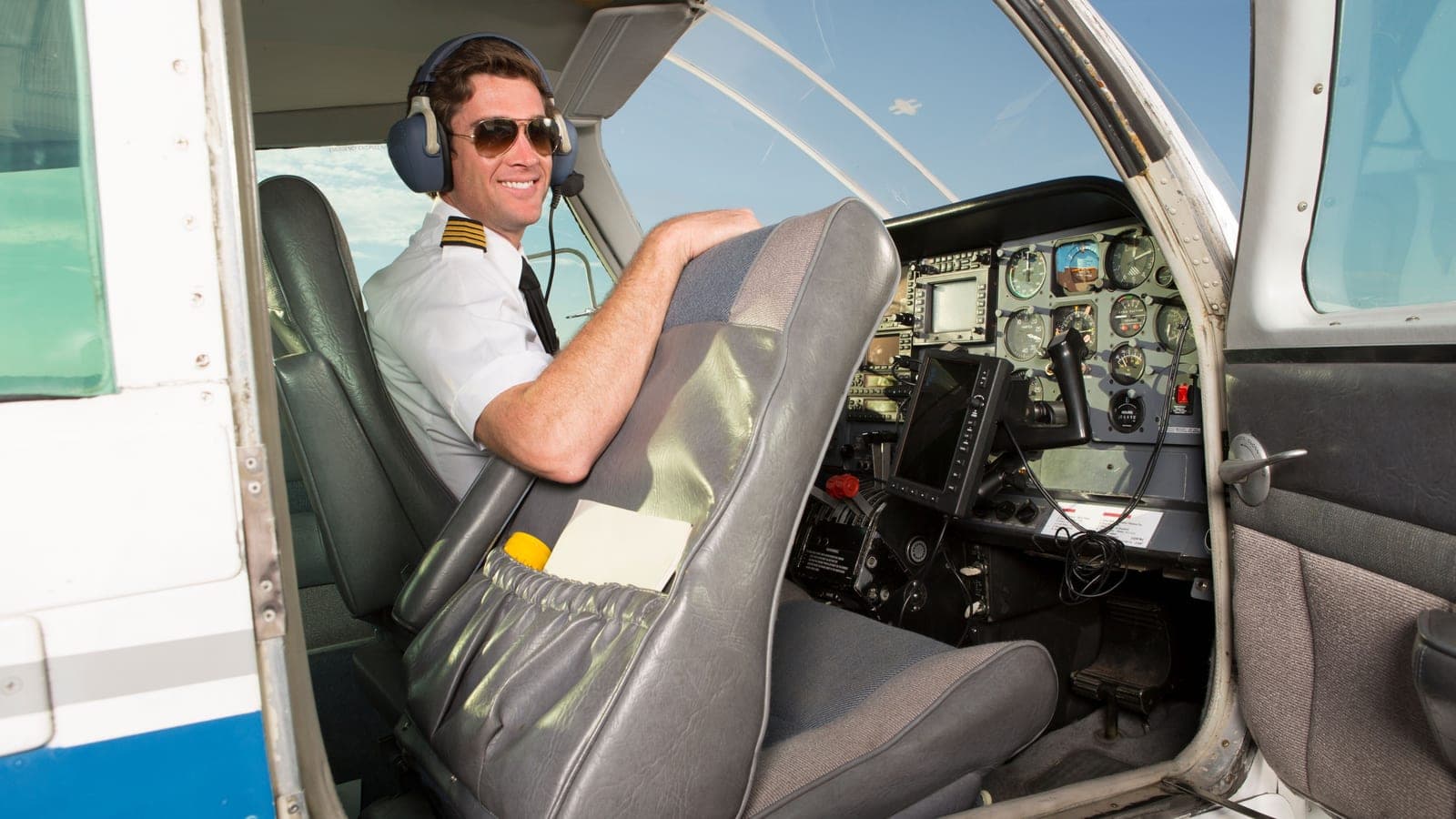A lone instructor in the left seat of a light aircraft, turned toward the empty right seat beside him