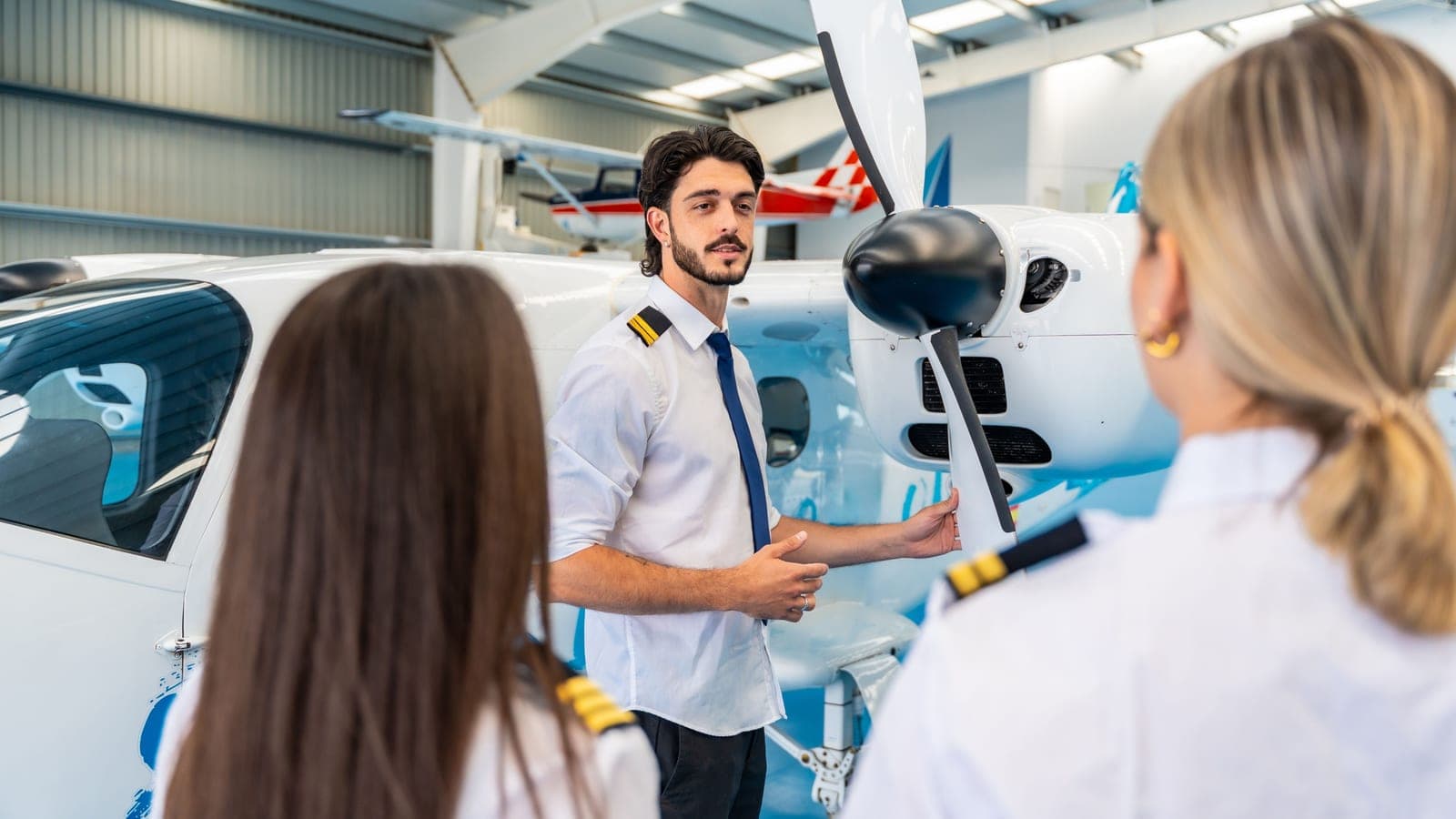 An instructor briefing two students beside an aircraft inside a hangar