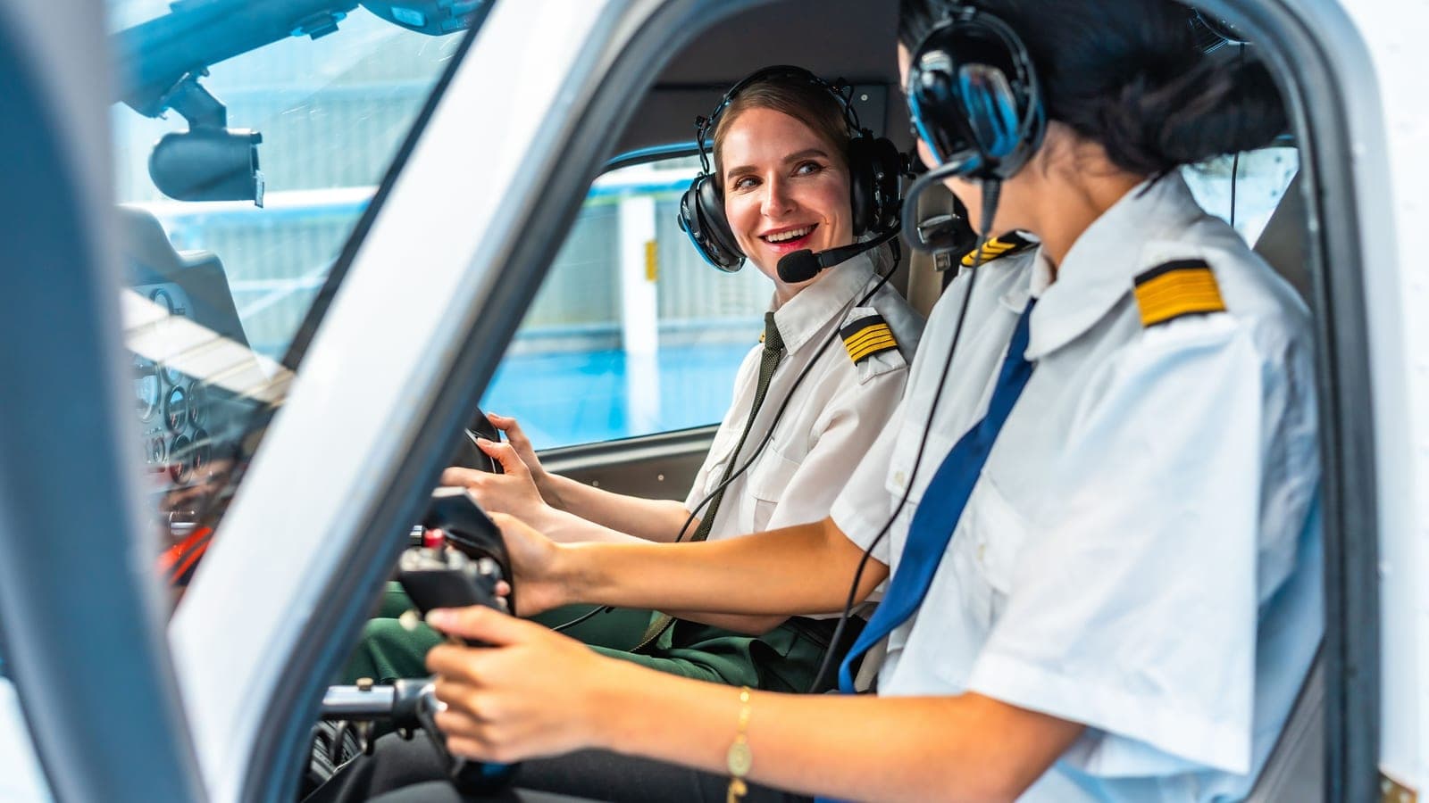 Two pilots at the controls of a light aircraft, one smiling over her shoulder